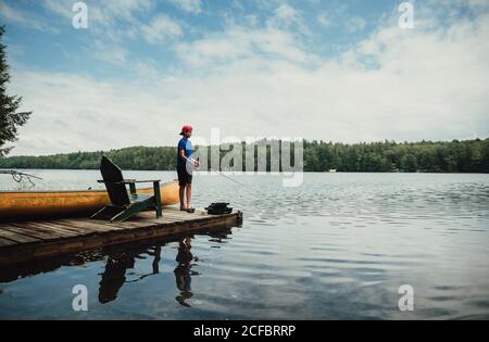 Teen boy fishing from a dock on a calm lake in the summer Stock