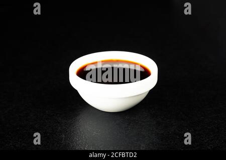 Soy sauce in a white saucer on a black background. For the restaurant menu. Traditional Chinese classic soy sauce. Sushi, Japanese cuisine Stock Photo