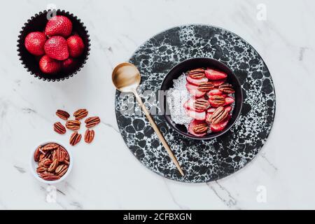 Top view of yummy sorbet with fresh strawberries and walnuts served in bowl on marble table near spoon Stock Photo