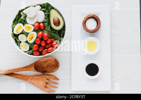 Served bowl of salad with spinach eggs avocados tomatoes and mozzarella cheese on table with condiments sauces Stock Photo