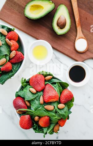 Bowls with strawberry almond and greenery on table with avocados and spoon of sauce on cutting board Stock Photo