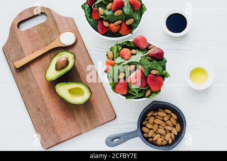 Bowls with strawberry almond and greenery on table with avocados and spoon of sauce on cutting board Stock Photo