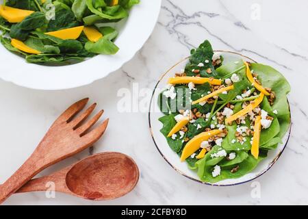 From above of bowl with healthy organic salad of green spinach topped with thin slices of pumpkin and goat cheese with walnuts Stock Photo