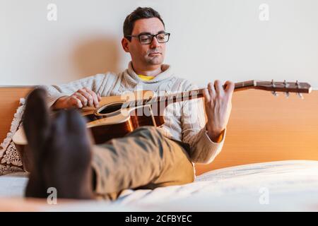 man playing the guitar on the bed of his house Stock Photo