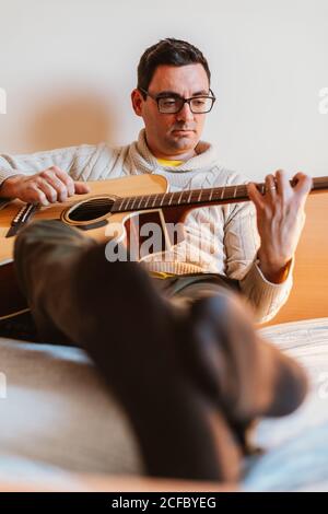 man playing the guitar on the bed of his house Stock Photo