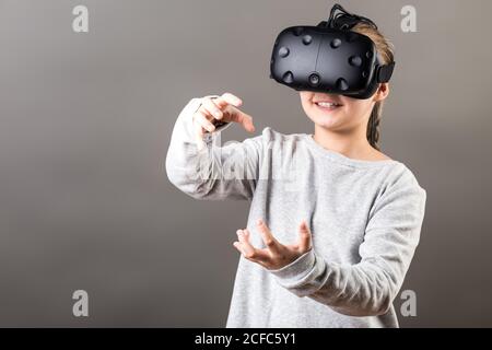 Child with virtual reality headset sculpts hands on grey background Stock Photo