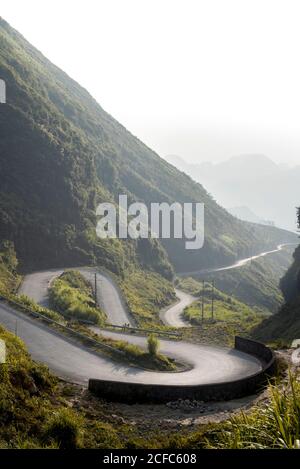 Spectacular landscape of winding paved route in green tropical highlands during foggy morning in summer Stock Photo