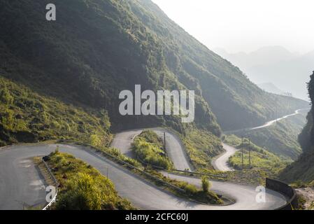 Spectacular landscape of winding paved route in green tropical highlands during foggy morning in summer Stock Photo