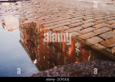 Reflection of old red building in water of puddle on cobblestone pavement of street, New York Stock Photo