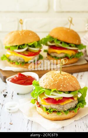 Delicious burgers, hamburger sandwich with cutlet, cheese, bacon and tomatoes on a wooden table. Stock Photo
