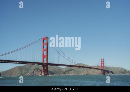 Famous suspension Golden Gate Bridge in San Francisco in California with hilly coast and clear blue sky in background in sunny day Stock Photo