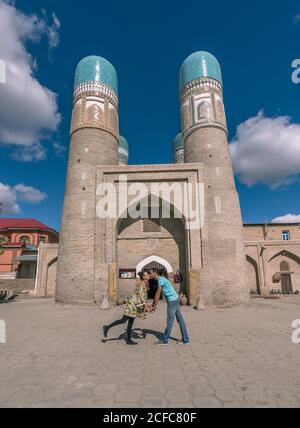 Side view of ethnic man and Woman holding hands and kissing each other while standing outside traditional Islamic building in Bukhara, Uzbekistan Stock Photo
