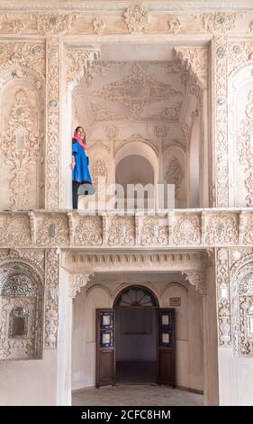 Side view of Muslim Woman in traditional clothes standing on terrace and leaning back on column of beautiful Iranian building with decorative ornaments Stock Photo