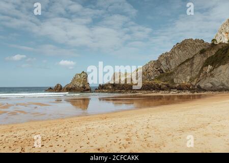 Magnificent view of tranquil ocean and sand beach with footprints near big rock in afternoon under blue sky with clouds Stock Photo