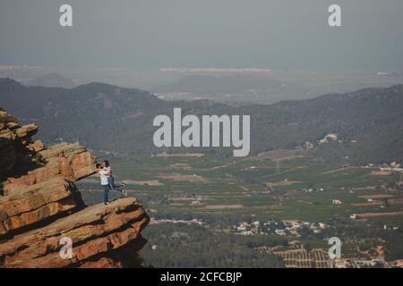 Distant loving couple embracing while standing on high cliff Stock Photo