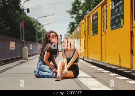 Beautiful young women sitting on train platform on summer day in Berlin looking at camera Stock Photo