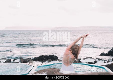 Young Woman with closed eyes resting in water of pool near rocks and cloudy sky Stock Photo