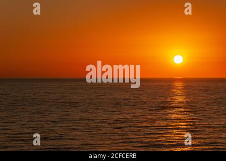 Cabo San Lucas, Mexico - November 23, 2008: Red sky sunset above dark Pacific Ocean reflecting orange sun in the evening. Stock Photo