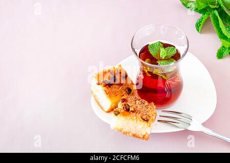 Glass of moroccan mint tea with Basbousa (namoora) traditional arabic semolina cake with almond nut and syrup. Copy space. Selective focus. Pink backg Stock Photo