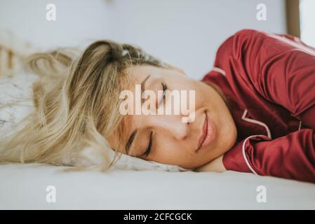 Young pretty Woman in pajamas smiling while sleeping on bed in bedroom Stock Photo