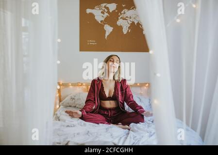 Young pretty Woman in pajamas sitting on bed with eyes closed Stock Photo