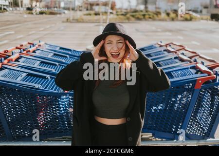 Attractive young Woman with red hair in black hat and jacket gesturing and screaming in parking lot with Stock Photo