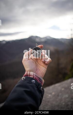 Crop man in jacket holding modern compass in outstretched hand while standing at rocky area Stock Photo