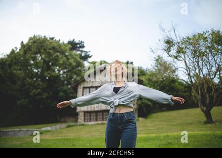 Casual calm young Woman dancing enjoying stroll on green meadow near wooden house in rural village in Asturias, Spain Stock Photo