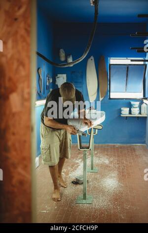 Woodworker diligently skinning surfboard in workshop Stock Photo