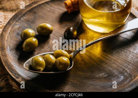 Glass jar with extra virgin oil placed on wooden plate with black and green olives Stock Photo