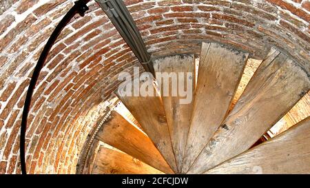 Looking down an old wooden spiral staircase in a brick circular turret in an old medieval brick church tower. Stock Photo