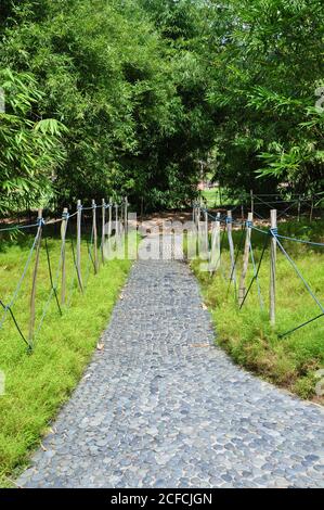Perspective view of a cobbled stone sensory footpath made of smooth rounded pebbles, with a rustic rope fence in a rural botanical garden setting. Stock Photo