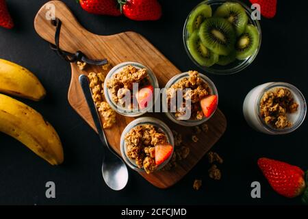 From above arrangement of bananas, bowl of sliced kiwi, milk bottles with walnuts and strawberry on black background Stock Photo