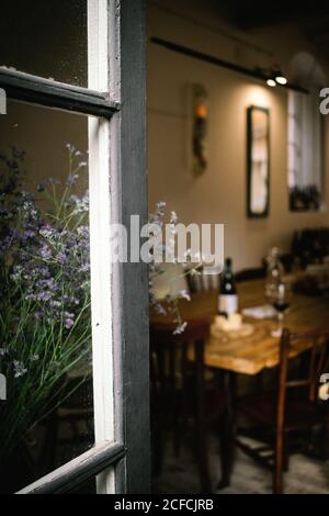 Fragment of interior of rustic restaurant with wooden table served with wine and cheese seen from open window with flowers Stock Photo