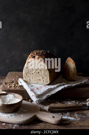 Loaf of delicious rye bread with seeds lying on timber tabletop near raw flour Stock Photo