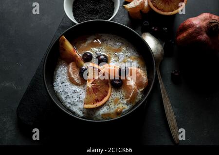 From above chia seeds pudding with slices of orange, mandarins and olives in bowl near spoon and grapefruit on dark table Stock Photo