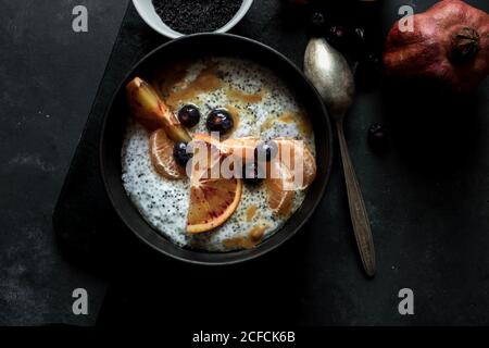 From above chia seeds pudding with slices of orange, mandarins and olives in bowl near spoon and grapefruit on dark table Stock Photo