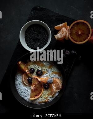 From above chia seeds pudding with slices of orange, mandarins and olives in bowl near spoon and grapefruit on dark table Stock Photo