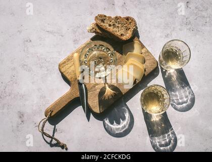 Top view composition with glasses of wine served with sliced cheese and bread with jam on marble table with wooden board in sunlight Stock Photo