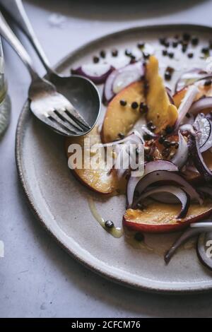 From above plate with gourmet salad made of peaches, red onion, oil and black pepper on white background Stock Photo