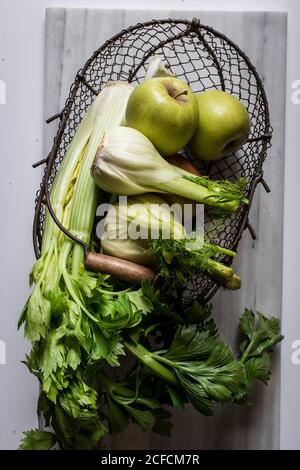 From above metal basket with apples, celery, fennel bulbs and walnuts arranged on board against white background Stock Photo