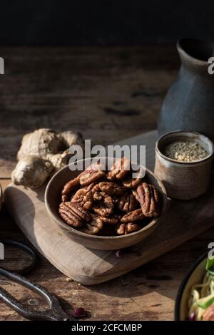 Bowl with pecan nuts near scissors, cutting board, pitcher and ginger in darkness Stock Photo