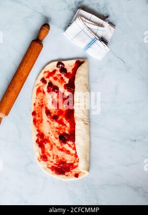 From above fresh strawberry brioche on the making placed near rolling pin and kitchen utensils on white modern marble table Stock Photo