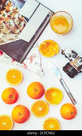 Flat lay of whole and halved oranges with cooking book and vintage photo camera on white table Stock Photo