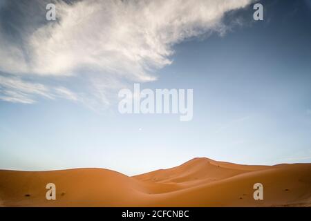 Small white cloud floating on blue sky over wonderful sand dune on sunny day in Morocco Stock Photo