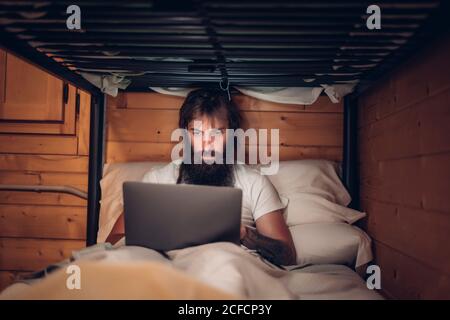 man using laptop in rustic bunk bed Stock Photo
