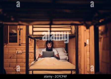 man using laptop in rustic bunk bed Stock Photo