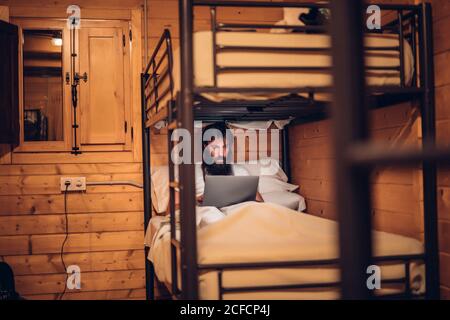 man using laptop in rustic bunk bed Stock Photo