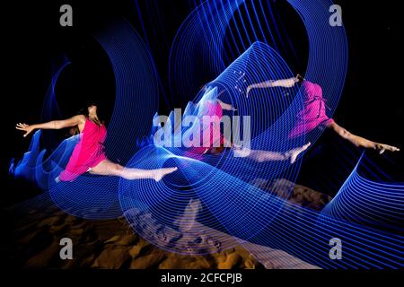 Tracks of blue neon light curling over barefoot dancing Woman on background of dark desert at night in Morocco Stock Photo