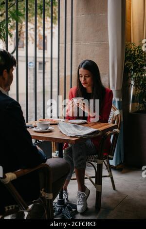 Calm relaxed young couple sitting at table next to window and drinking coffee and talking while having breakfast in cafe Stock Photo